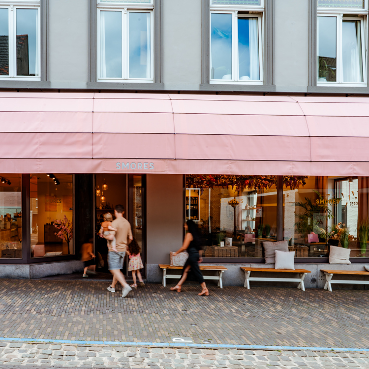 Twee ouders en twee kinderen gaan met het gezin een winkel binnen met roze luifels in Meerssen