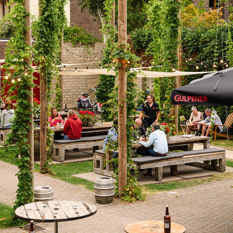 Mensen zitten op het terras van het brouwlokaal van gulpener en drinken bier op picknicktafels