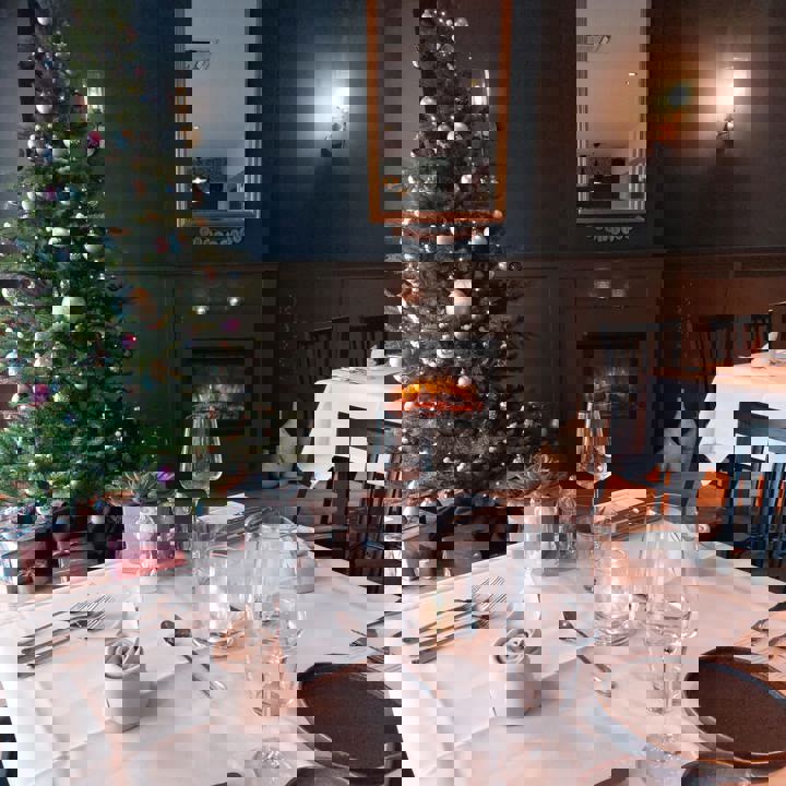 Gedekte tafel in restaurant met een kerstboom en openhaard op de achtergrond.