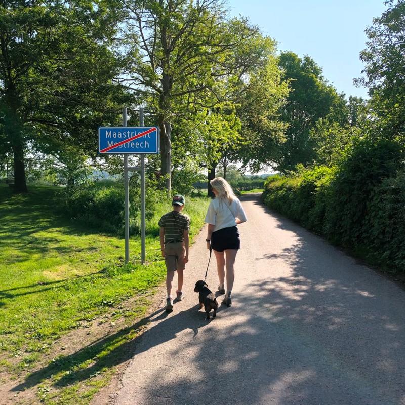 Moeder, zoon en hondje wandelen het bord van Maastricht voorbij, voor een wandeling in het groen.