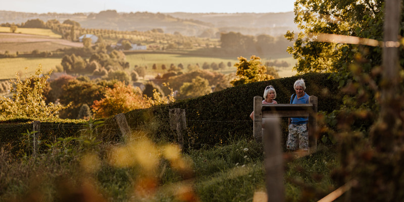 Twee wandelaars lezen het wijnbord van Wijngoed Aldenborgh met Toscaans uitzicht over de heuvels