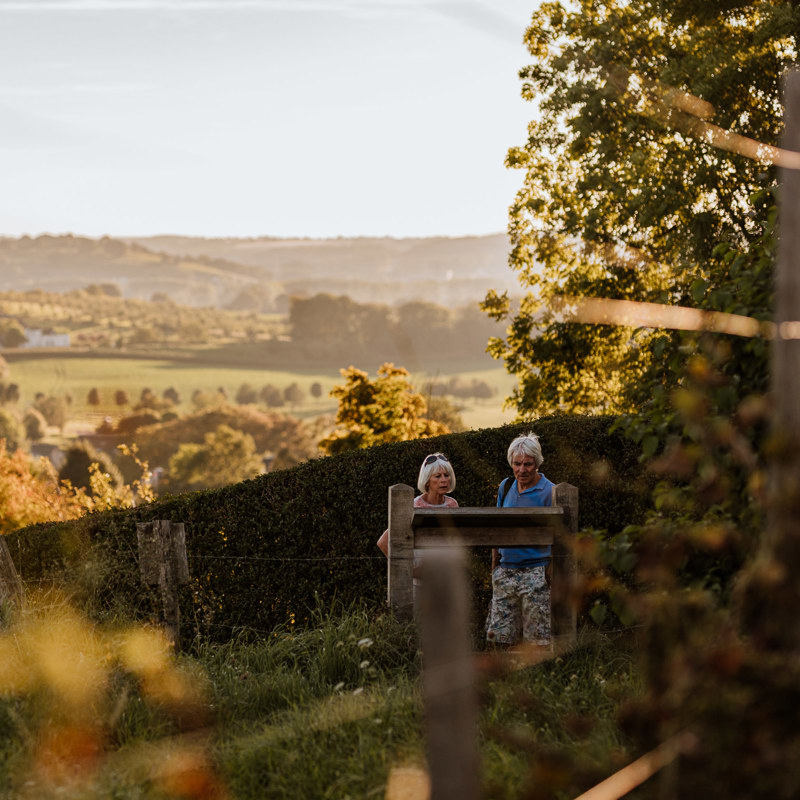 Twee wandelaars lezen het wijnbord van Wijngoed Aldenborgh met Toscaans uitzicht over de heuvels