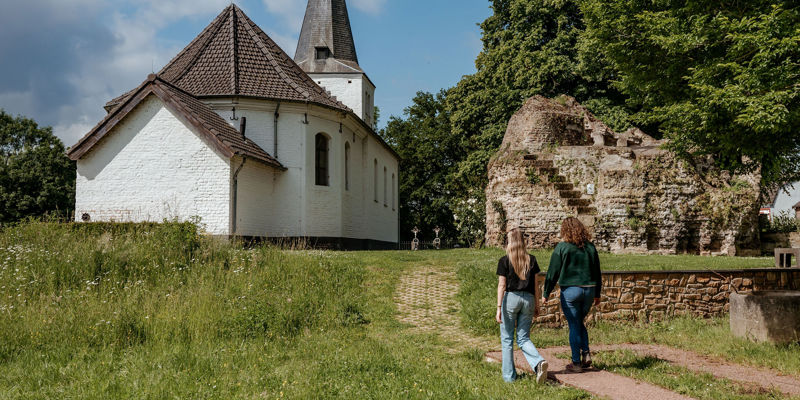 Twee dames wandelen richting een klein wit kerkje. 