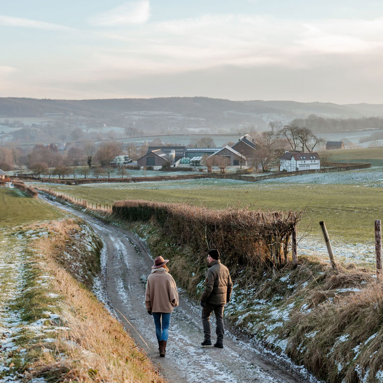 Koppel loopt op wandelpad naar beneden richting boerderijen in een winterse omgeving