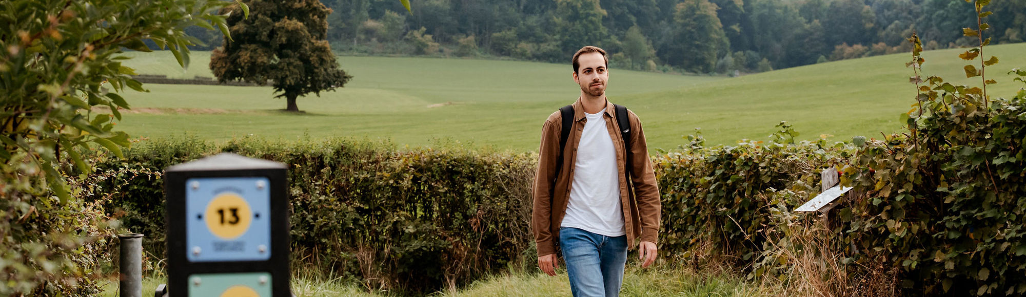 Een jonge man wandelt door het heuvellandschap langs een knooppuntenpaaltje