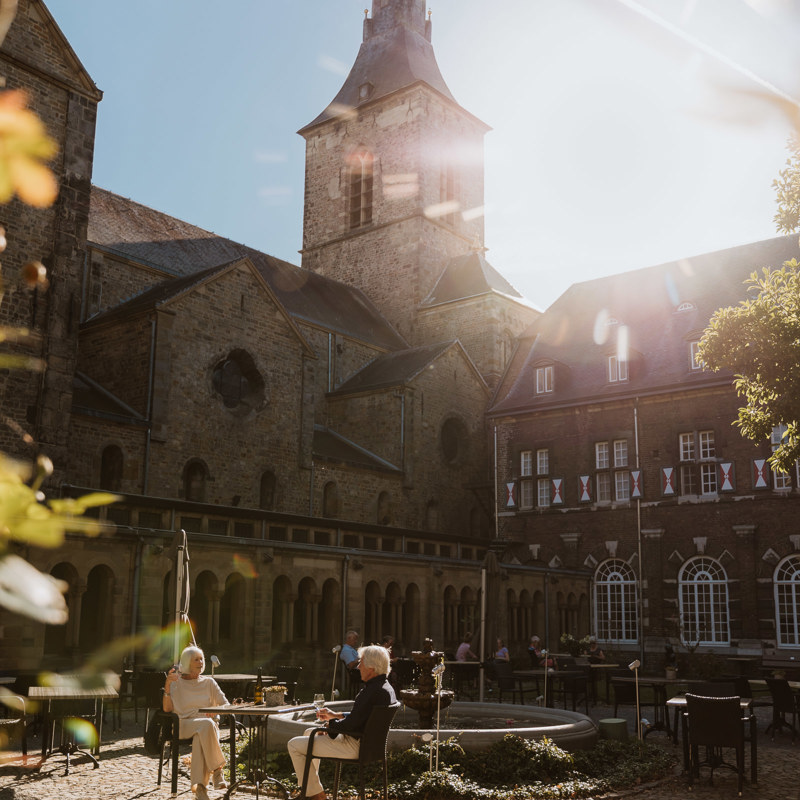 Een man en vrouw proosten met een glaasje wijn op het terras op de binnenplaats van Abdij Rolduc 