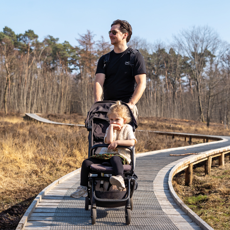 Vader met kindje in de kinderwagen wandelen over houten vlonder in het Schutterspark.