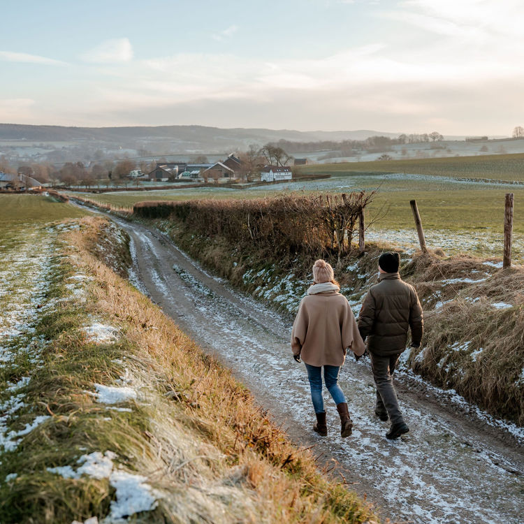 Koppel loopt op wandelpad naar beneden richting boerderijen in een winterse omgeving