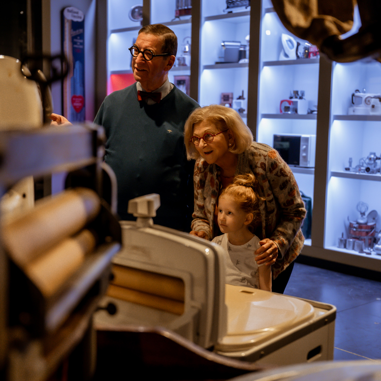 Opa en oma met kleinkind kijken naar een tentoonstelling van het discovery museum in kerkrade met apparaten op de achtergrond