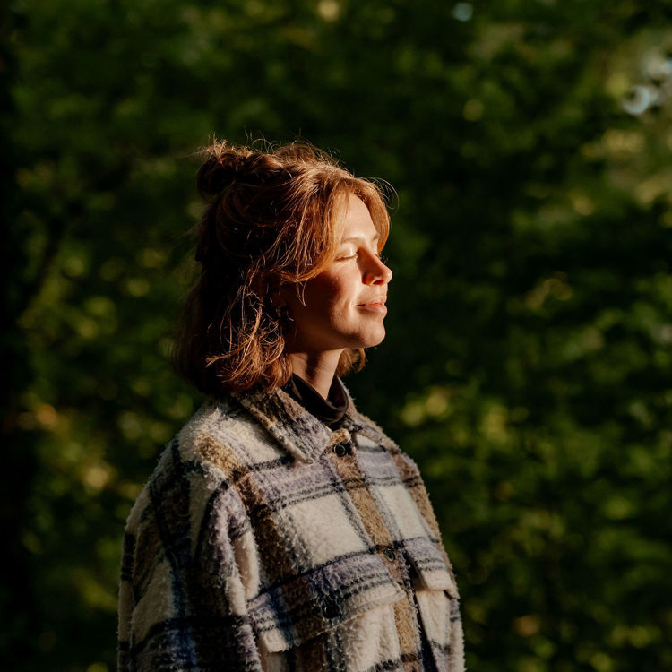 Jonge vrouw geniet van de avondzon op haar gezicht in een natuurrijke omgeving.