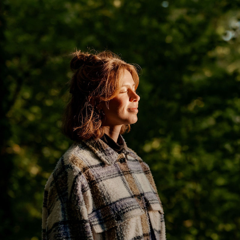 Jonge vrouw geniet van de avondzon op haar gezicht in een natuurrijke omgeving.