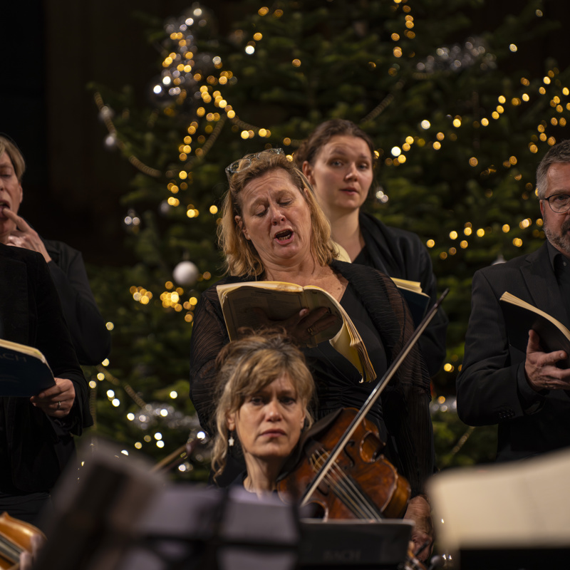 Orkest en koor zingen en spelen muziek voor een kerstboom met lichtjes