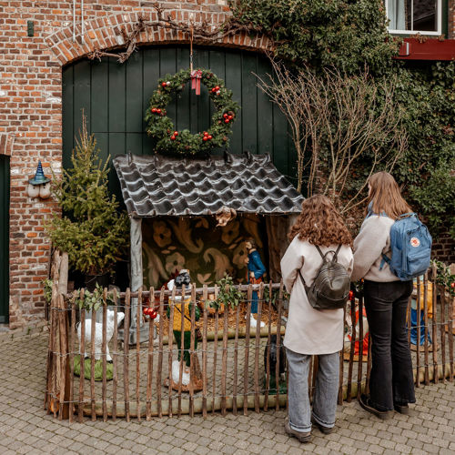 Twee dames met rugzak kijken naar een kerststalletje achter een hekje op een binnenplaats in Mechelen.
