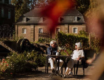 Een man en vrouw proosten aan een tafeltje voor de wijngaard van Abdij Rolduc