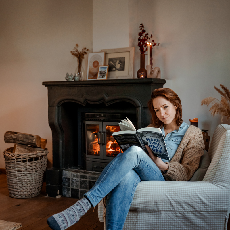 Persoon zitten op luie stoel die boek leest bij haardvuur
