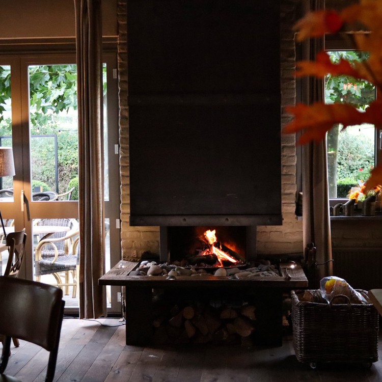 Brandende openhaard in een restaurant met herfstbladeren op de voorgrond en verschillende stoelen en tafels