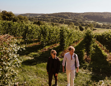 Twee wandelaars komen tussen de wijnranken van Wijndomein Guillaume vandaan